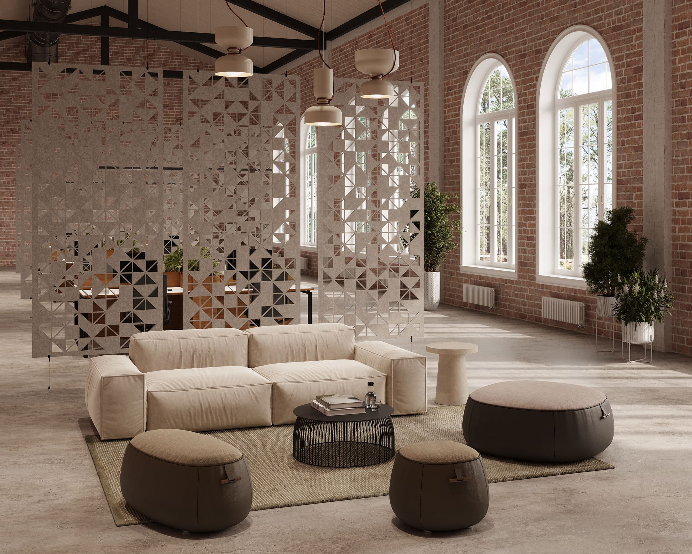 A modern industrial living space featuring a large cream sofa, a round black coffee table, and three gray ottomans. The room has high ceilings with exposed beams, brick walls, large arched windows, and acoustic felt screens as decorative partitions. Potted plants add greenery to the space.