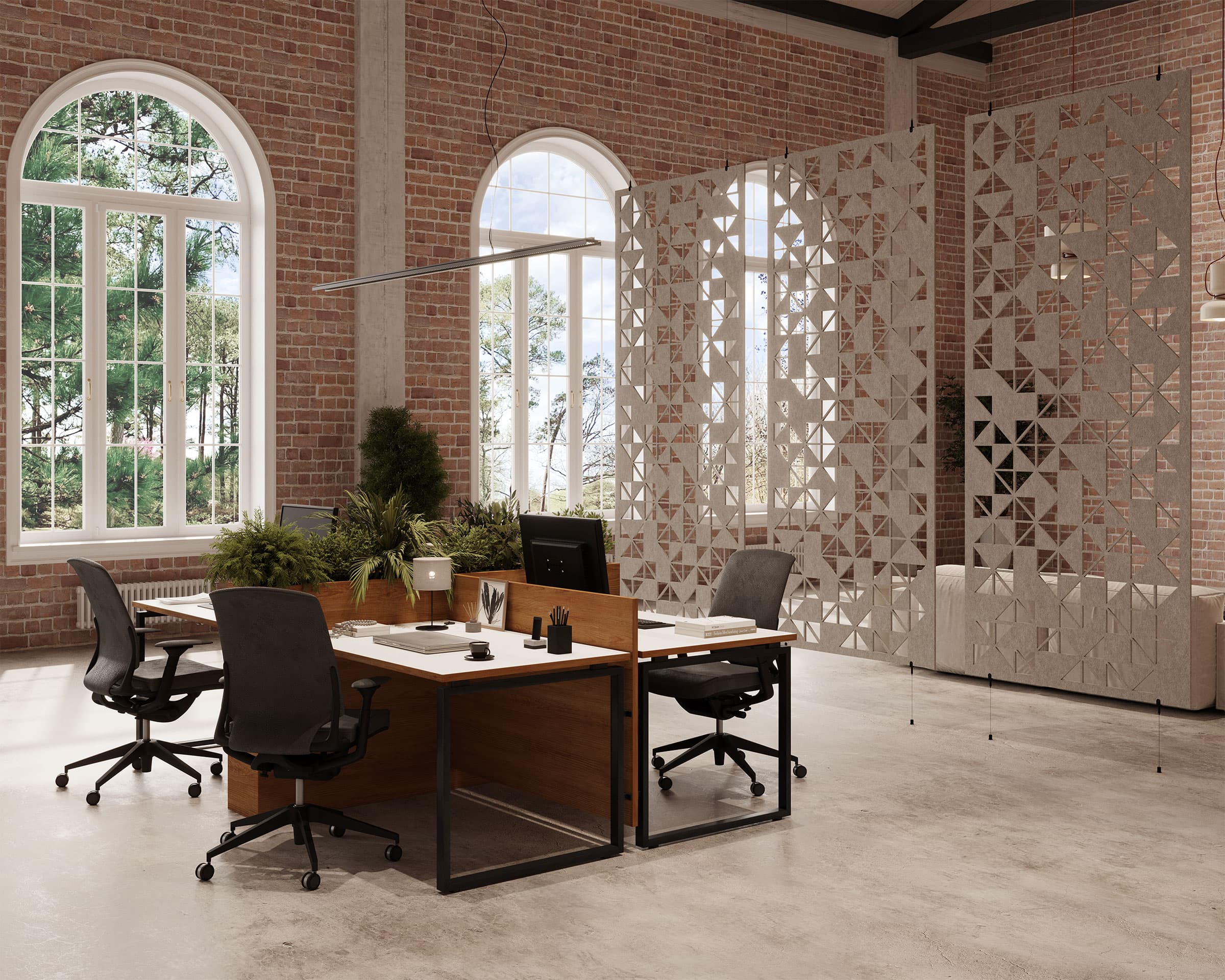 A modern office space with two desks facing each other, equipped with office chairs, computer monitors, and potted plants. The room features large arched windows, brick walls, and acoustic felt screens for decoration. Natural light fills the space, highlighting its minimalist decor.