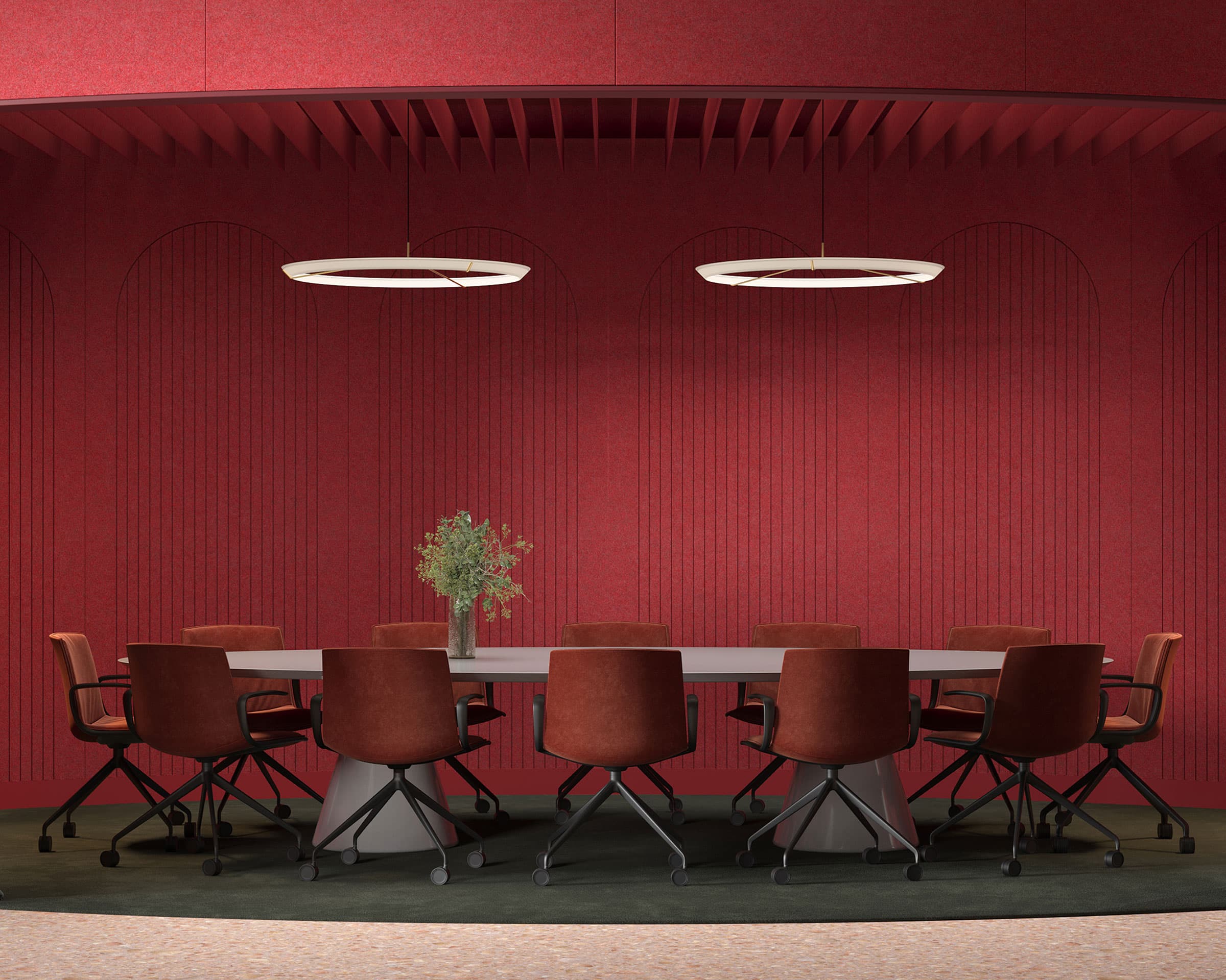 A modern conference room with a long rectangular table surrounded by eight brown swivel chairs. The room features a striking red wall adorned with arched patterns and arch acoustic felt wall panels, complemented by two circular overhead light fixtures. A small green plant is centered on the table.