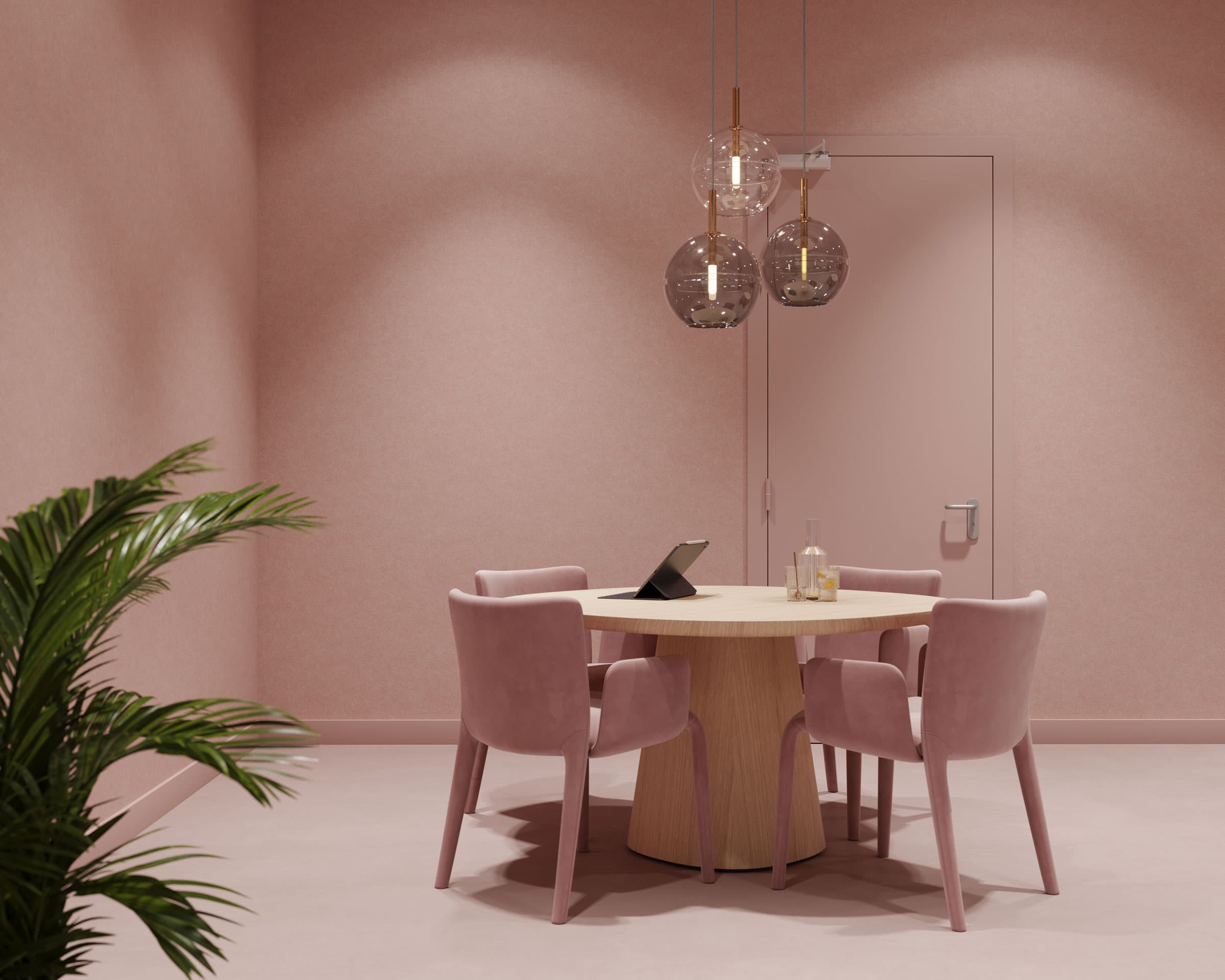 A small, elegant meeting room with a round wooden table surrounded by four pink upholstered chairs. The room features soft pink acoustic felt wall panels and a matching door. Above the table, three modern pendant lights hang while a potted plant is visible in the foreground.