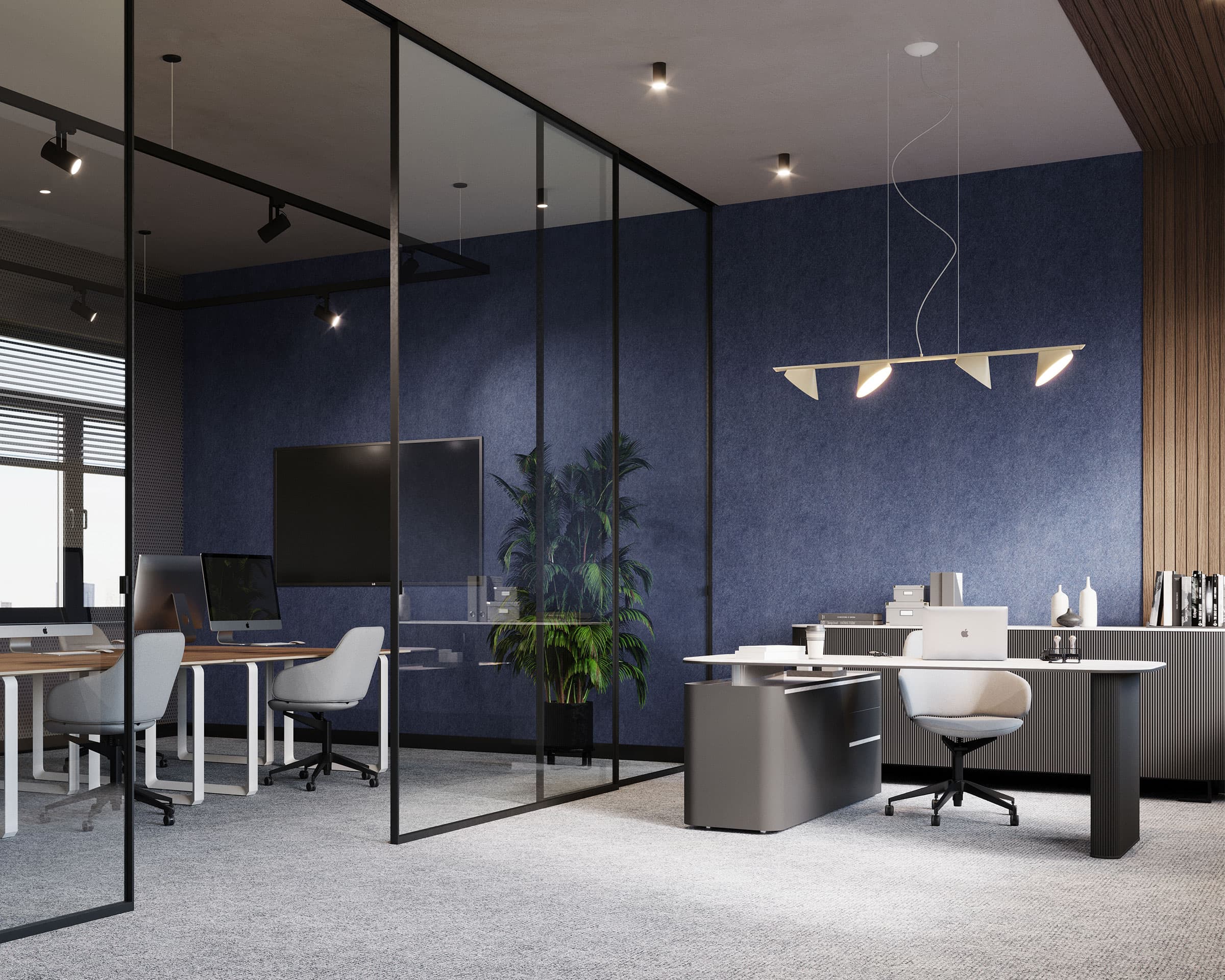 A modern office space with glass partitions dividing the area. The office features minimalist white desks, grey chairs, and a large flat-screen TV mounted on a blue acoustic felt accent wall. A tall plant adds a touch of greenery, while ceiling lights provide illumination.