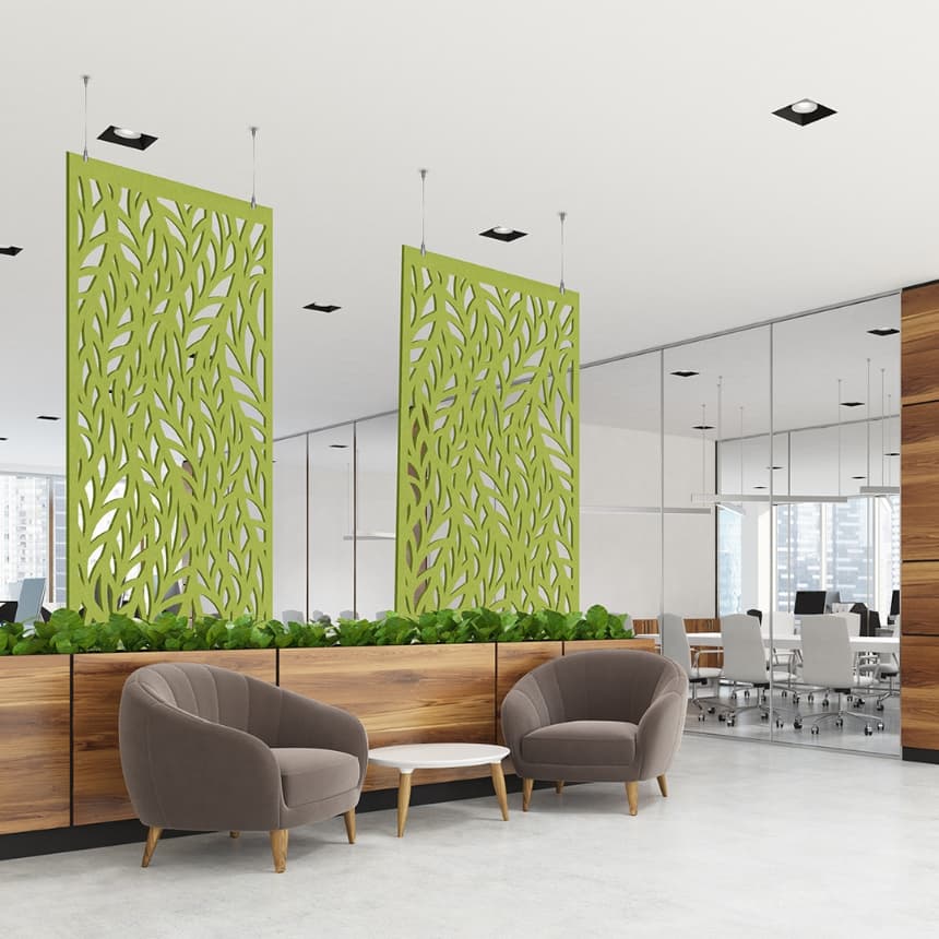 Modern open office space with two brown armchairs and a small white table in the foreground. Green leaf-patterned acoustic felt screens hang from the ceiling, separating the lounge area from the meeting space behind. Wooden planters with greenery add a natural touch.