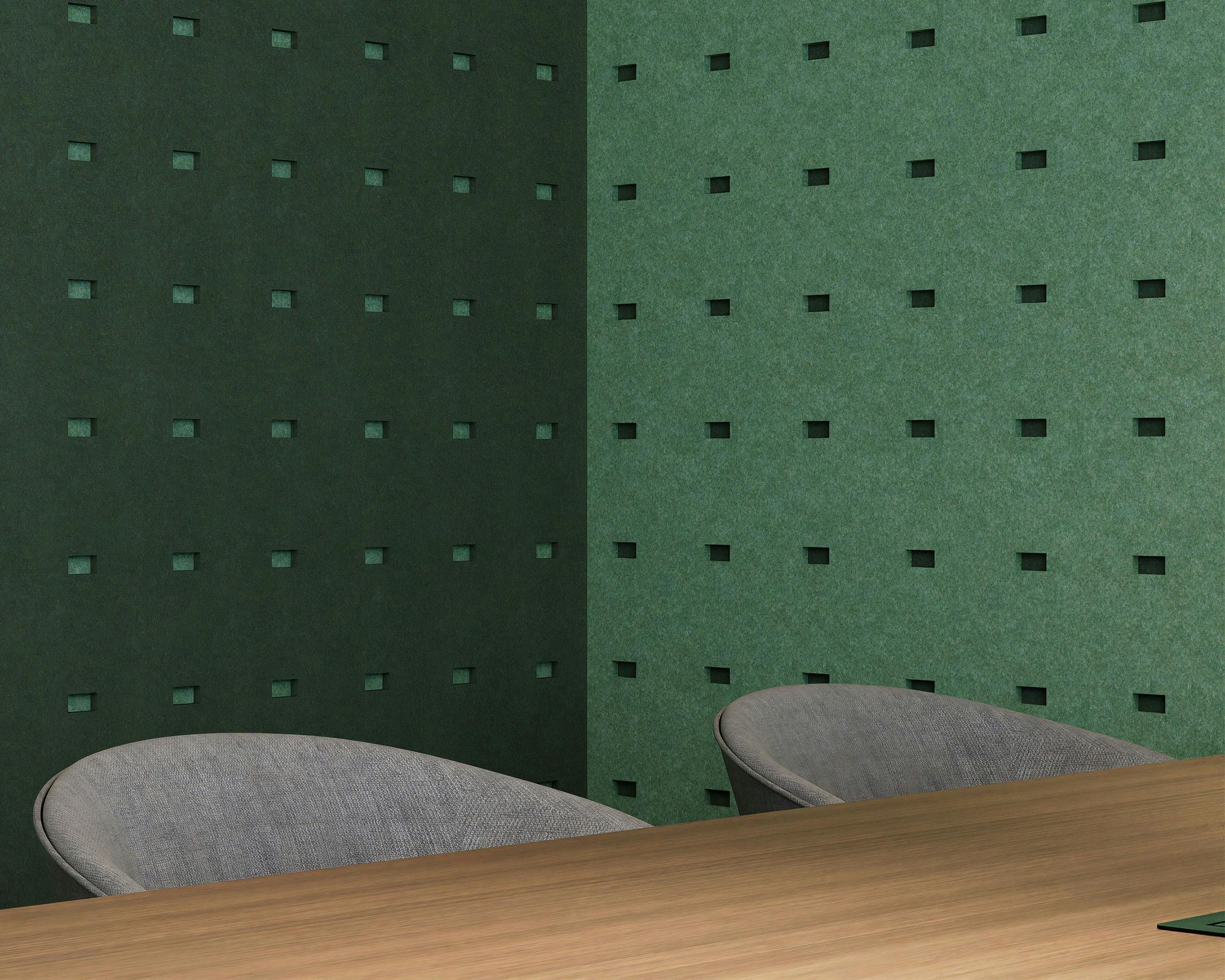 A modern office corner with dark green and light green walls featuring small rectangle cutouts in the acoustic felt wall panels. The room contains a wooden desk and two gray fabric chairs, with the minimalist design focusing on clean lines and a calming color palette.