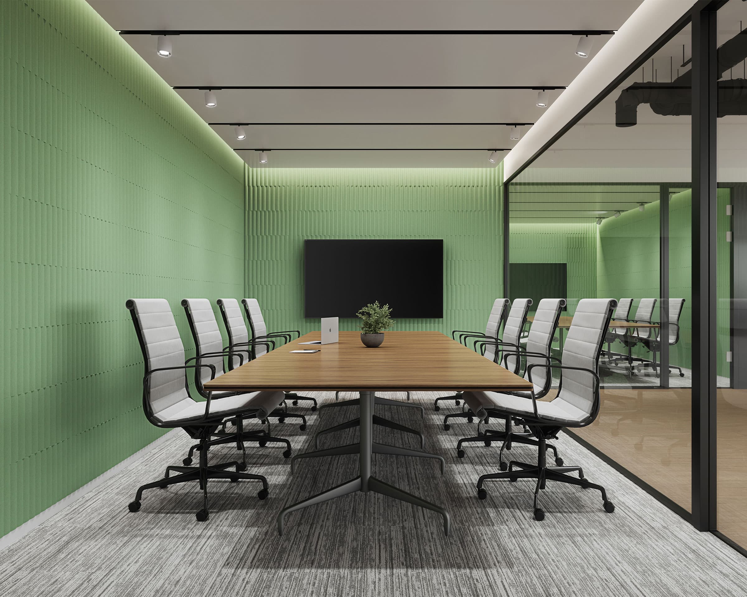 A modern conference room with a long wooden table surrounded by eight white chairs on wheels. The green walls feature stylish acoustic felt wall tiles, and a large flat-screen TV is mounted at the head of the table. Ceiling lights illuminate the room, and a glass partition is on one side.