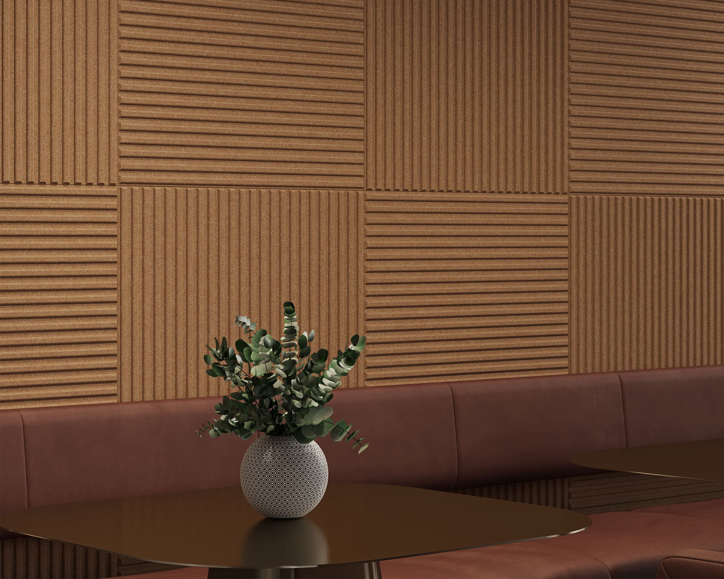 A modern seating area features brown acoustic felt wall tiles, a brown cushioned bench, and round dark tables. A round white vase with green foliage sits on one table, adding a touch of nature to the contemporary design.