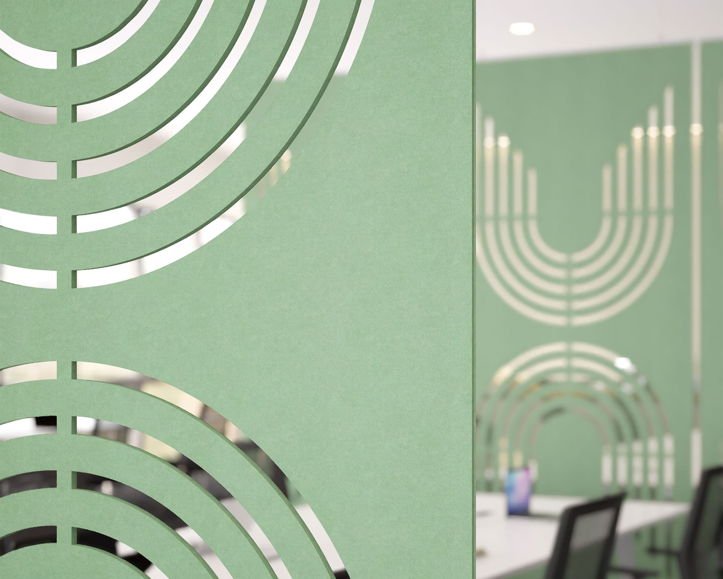 Close-up of a green office partition featuring circular cut-out patterns made from acoustic felt screens. In the background, a blurred image of a modern office space with green walls, mirrored elements, and chairs around a desk is visible. The design creates a cohesive, artistic ambiance.