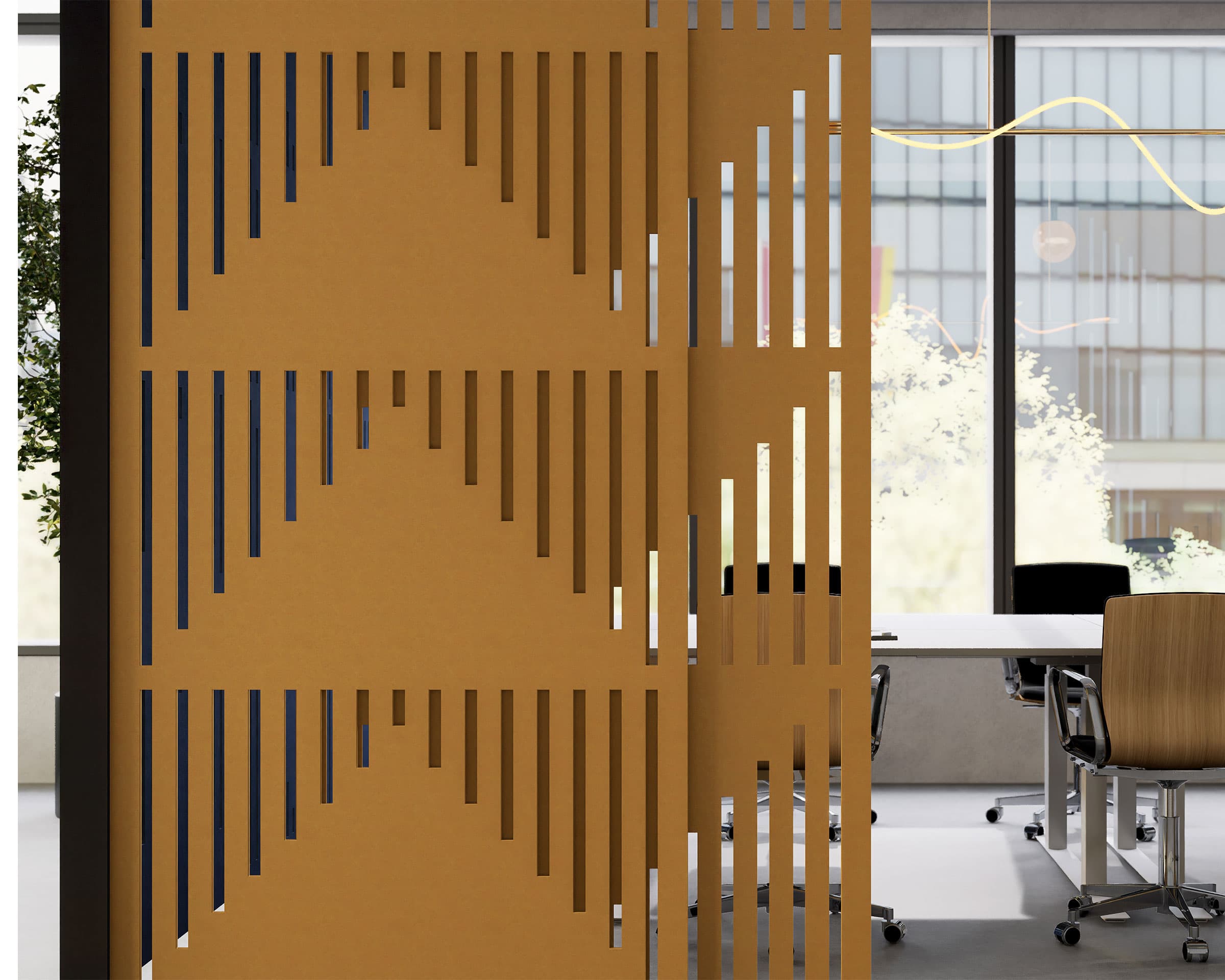 A modern office space features a decorative acoustic felt screen with vertical and diagonal slats, creating geometric patterns. Behind the partition are desks with chairs, large windows allowing natural light, and a potted plant on the left side.