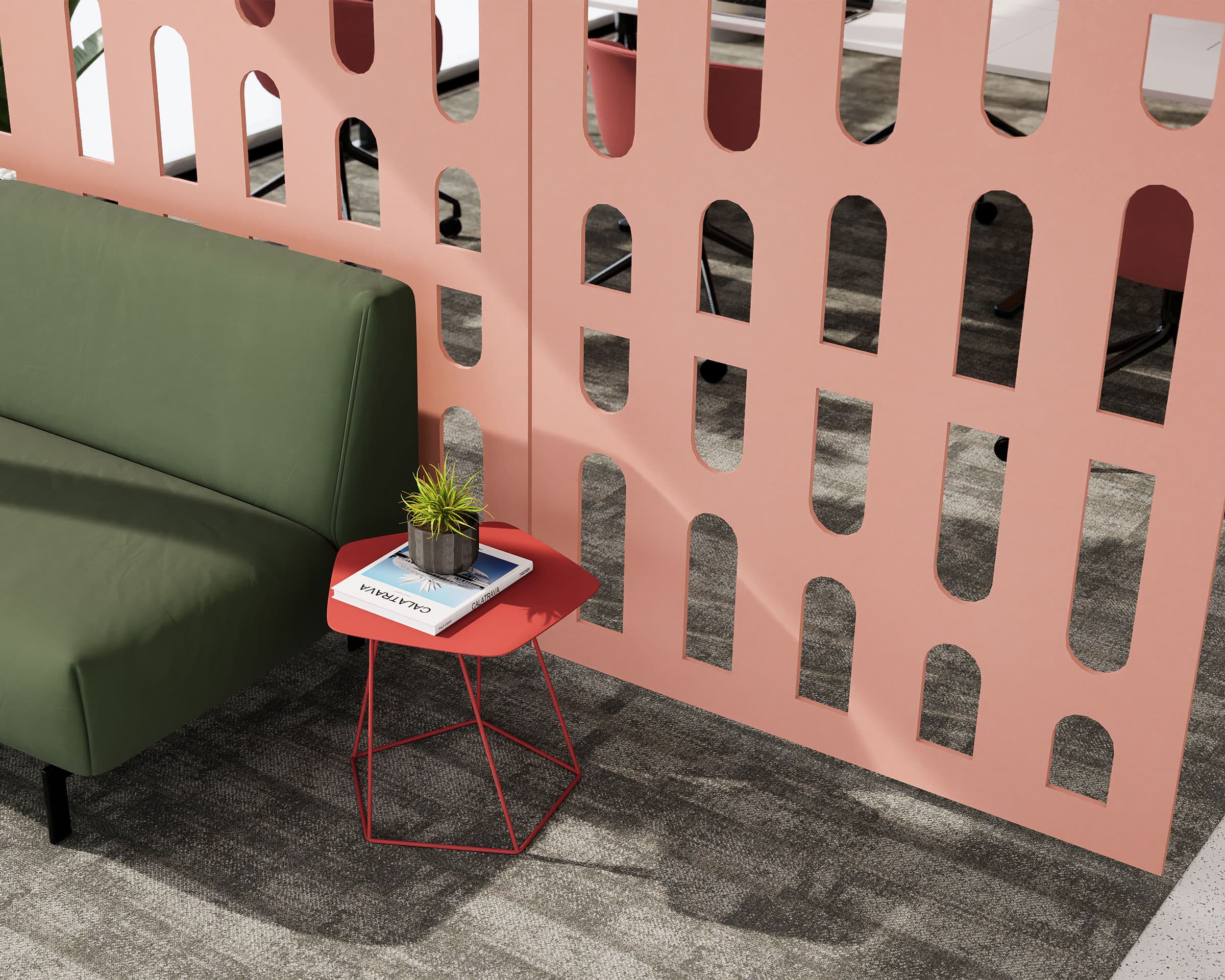 A green couch sits next to a small red table with a book titled “WORK HARD” and a small plant. The furniture is adjacent to a pink acoustic felt screen with various rectangular and curved openings. The area has gray carpet flooring and modern interior design.