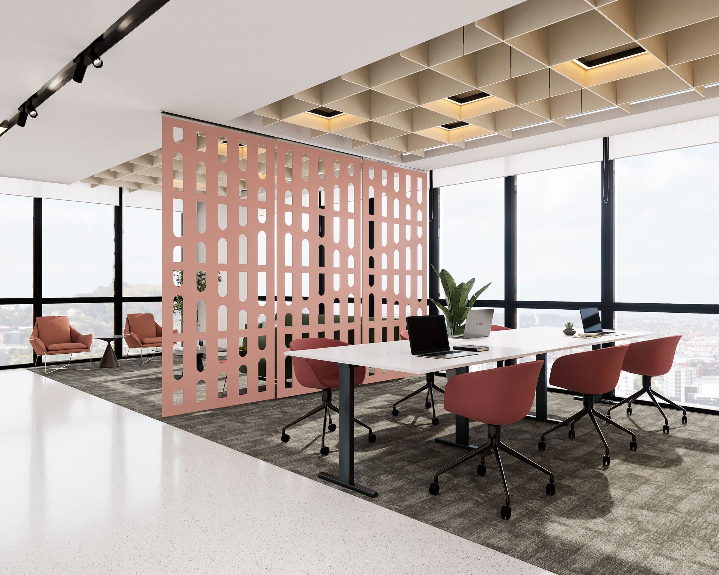 Modern office space featuring a white desk with red chairs, black laptops, and a green plant in the center. A pink, cutout acoustic felt screen stylishly separates the room. Large windows showcase a cityscape, and several red armchairs are placed in the background.