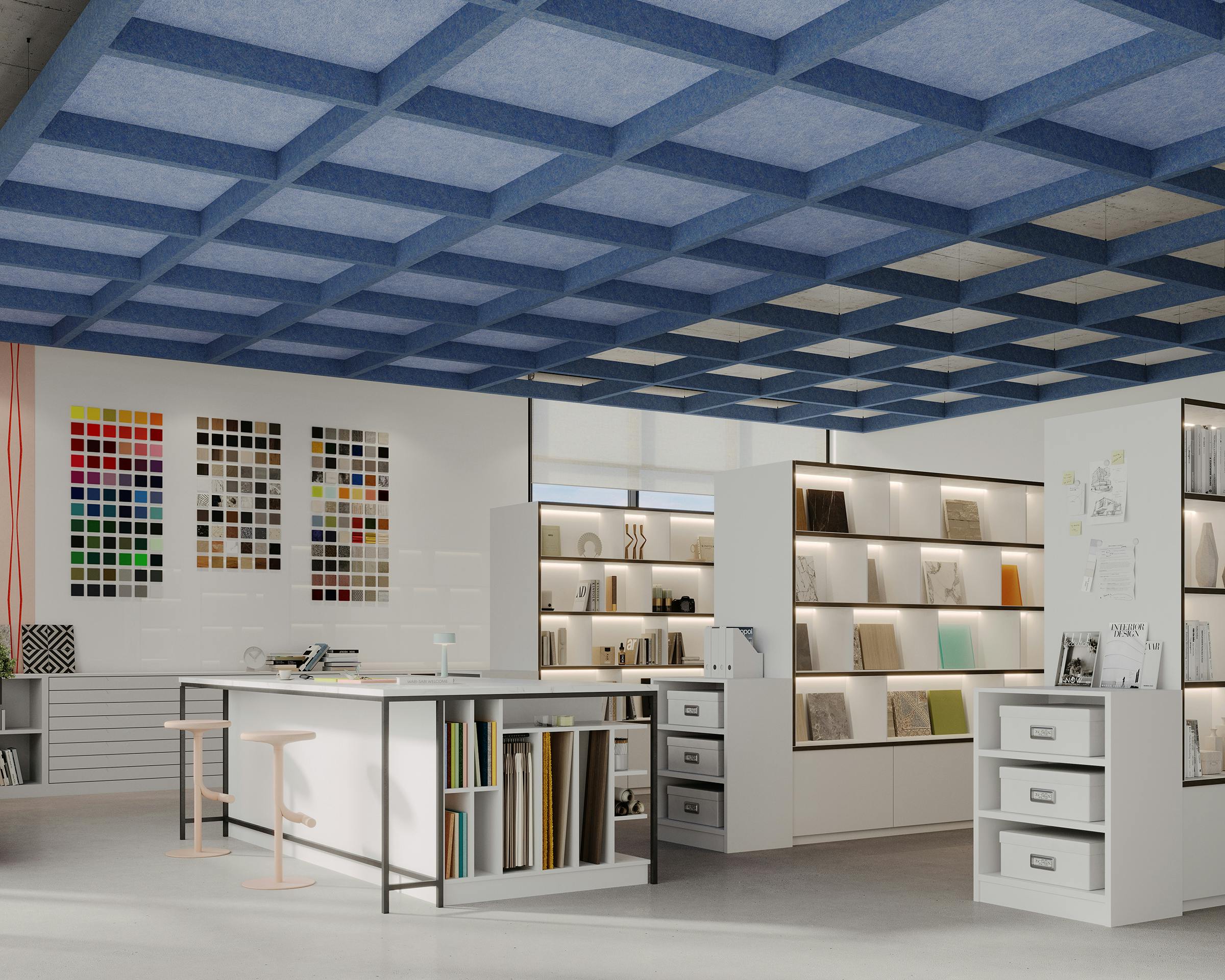 A modern interior design studio with white walls, ergonomic furniture, and a blue grid capped ceiling. The room features color swatch samples on the wall, shelving units with books and design materials, a large worktable with stools, and drawers for storage.