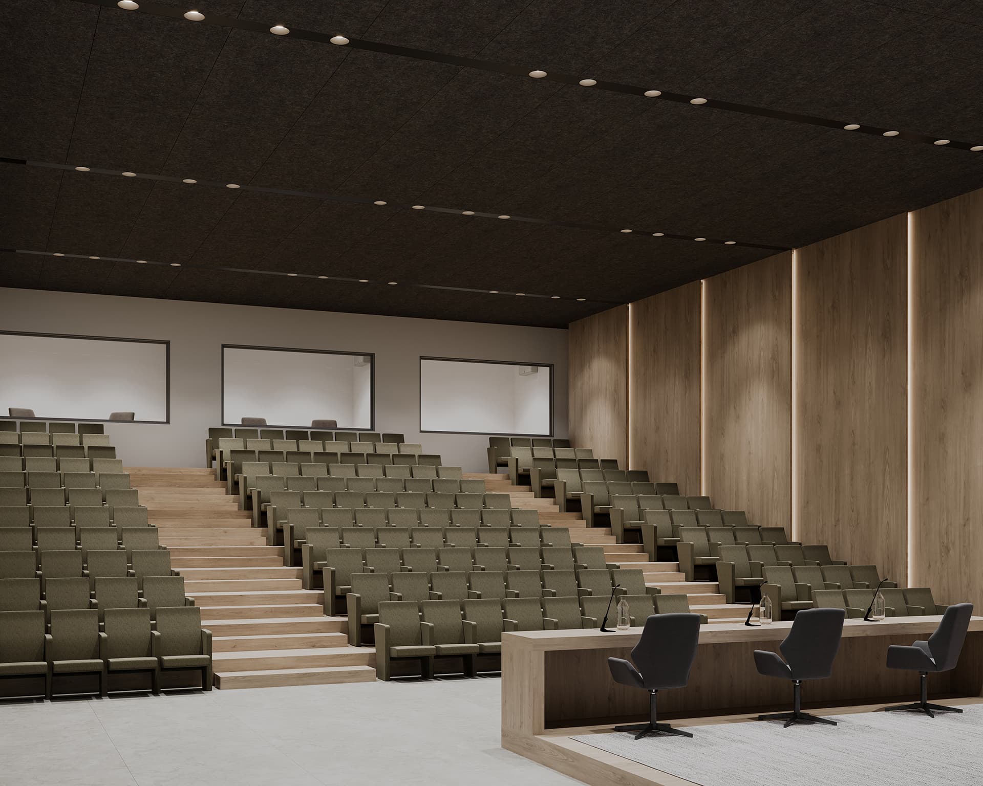 A modern, empty lecture hall with tiered seating upholstered in green fabric. The space features a wooden podium at the front with three microphones and chairs. The walls are lined with light wood paneling, and recessed lighting is installed in the ceiling.