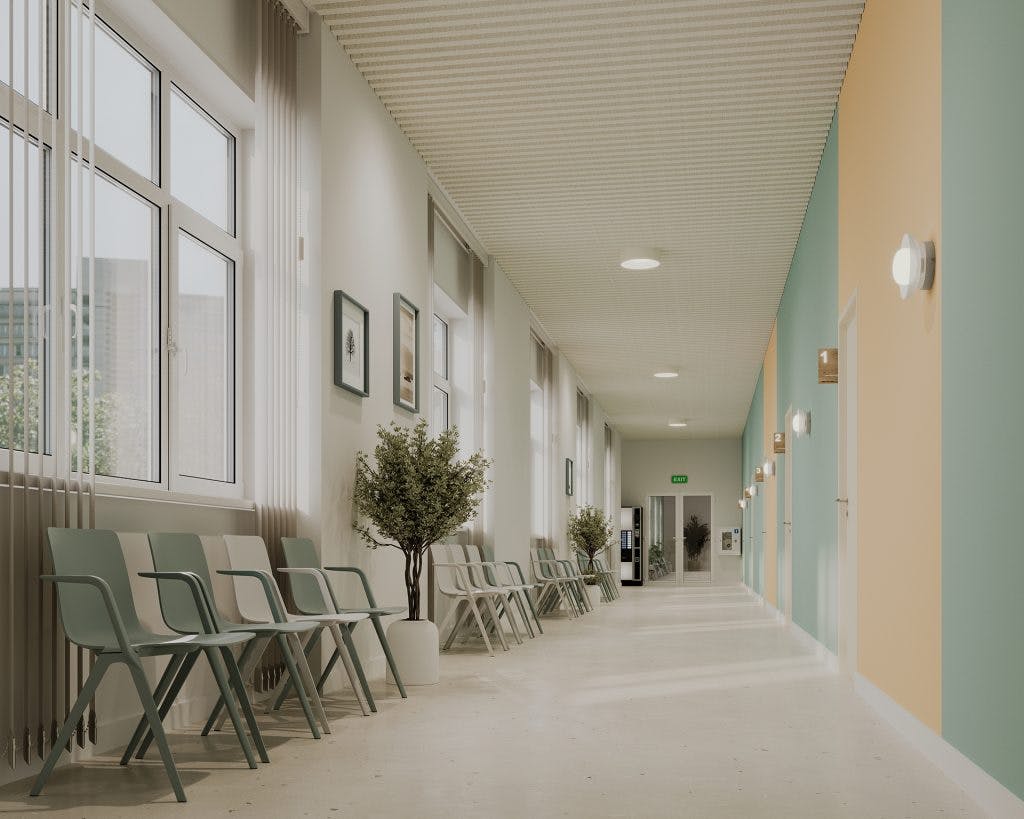 A brightly lit hallway with light green and yellow walls features an acoustic ceiling frame, modern chairs lined up on the left side, windows allowing natural light, potted plants, framed pictures, and wall-mounted lights. The clean, minimalist design creates a welcoming environment.