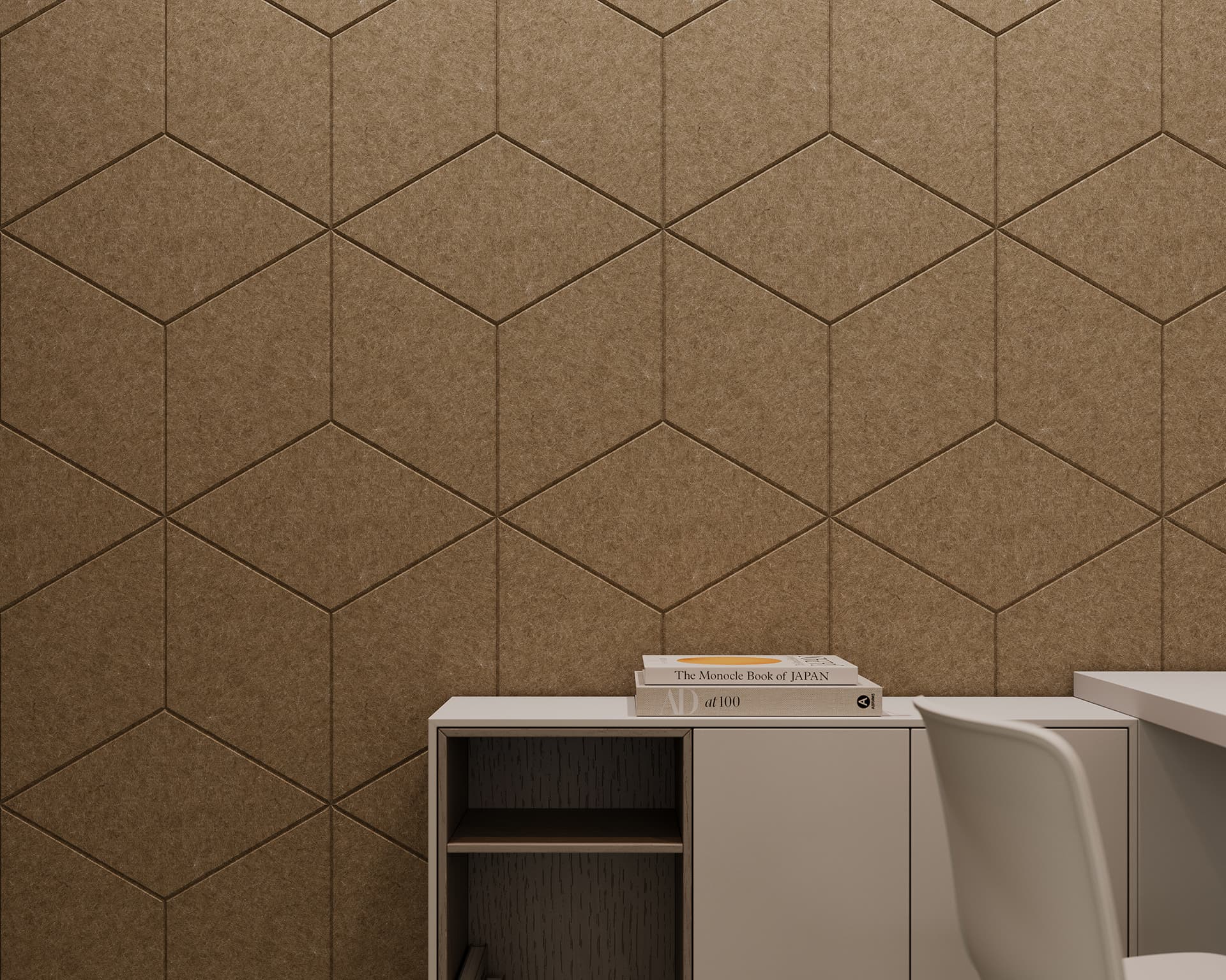 A modern office setup features a geometric-patterned acoustic felt wall in beige tones. In front of the wall is a white cabinet with open and closed sections along with several stacked books. A white chair is partially visible beside the cabinet.