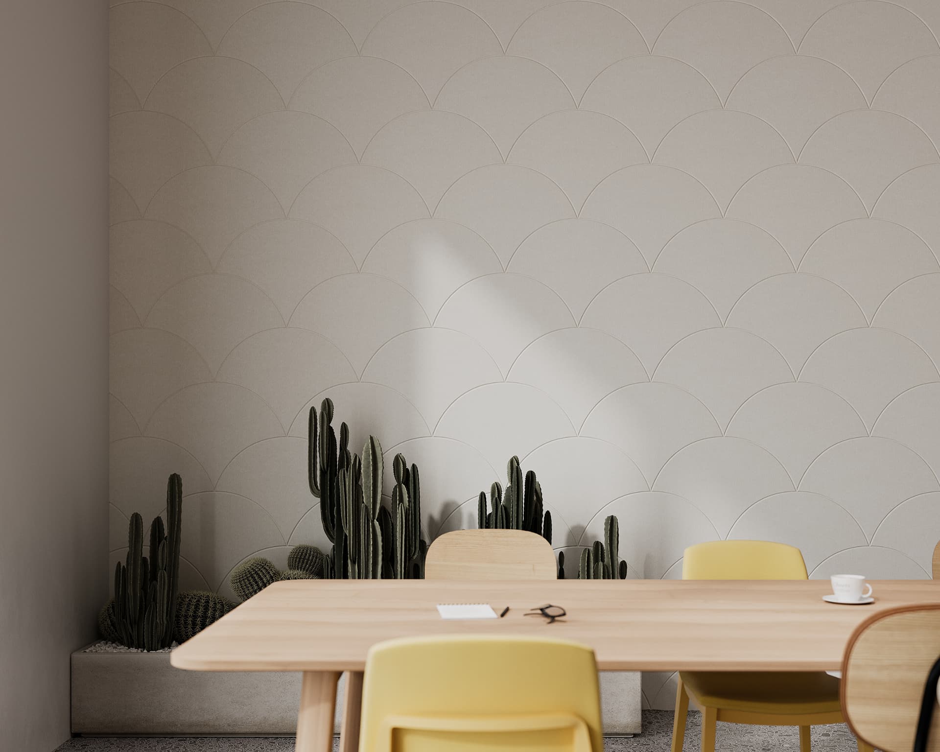 A minimalist room features a light wood table with a white coffee cup, a notebook, and a pencil. The acoustic wall has a scale pattern, and there are cacti plants in a planter along the base of the wall. Yellow chairs are placed around the table.