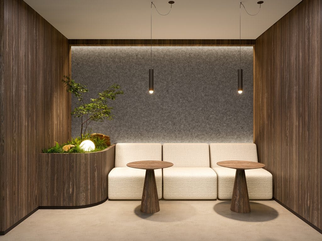 A modern minimalist waiting area with wooden walls, an acoustic felt wall, and a beige sofa. Two round wooden coffee tables are placed in front. A corner planter with greenery and a light adds a natural touch. Two pendant lights hang from the ceiling, providing soft illumination.