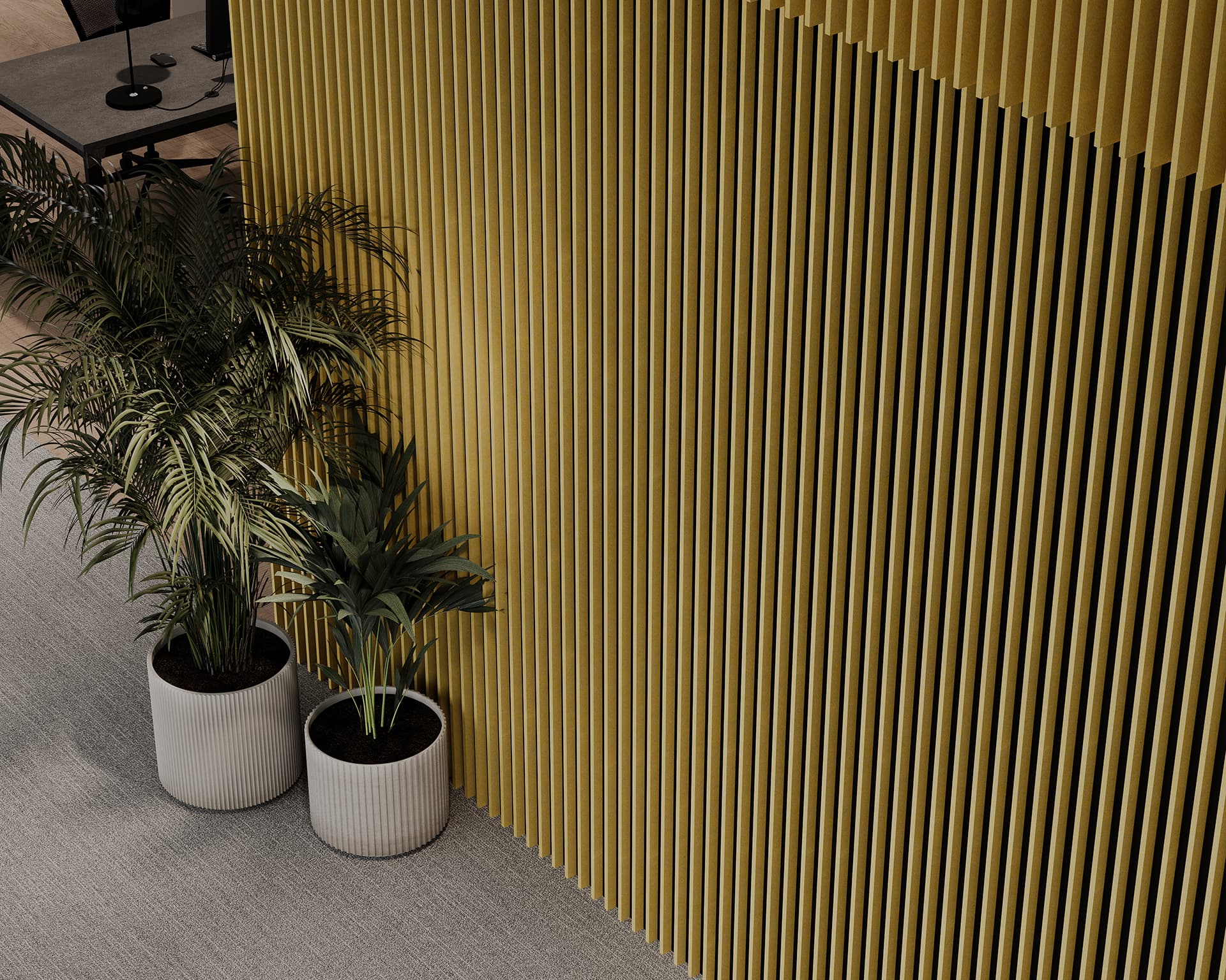 Two potted plants are placed beside a tall, wheat-yellow slatted acoustic felt panel. The floor is carpeted in a light gray color, and the edge of a workspace with chairs and desks is visible in the upper left corner of the image, creating an inviting environment for employees to prevent any potential injury.