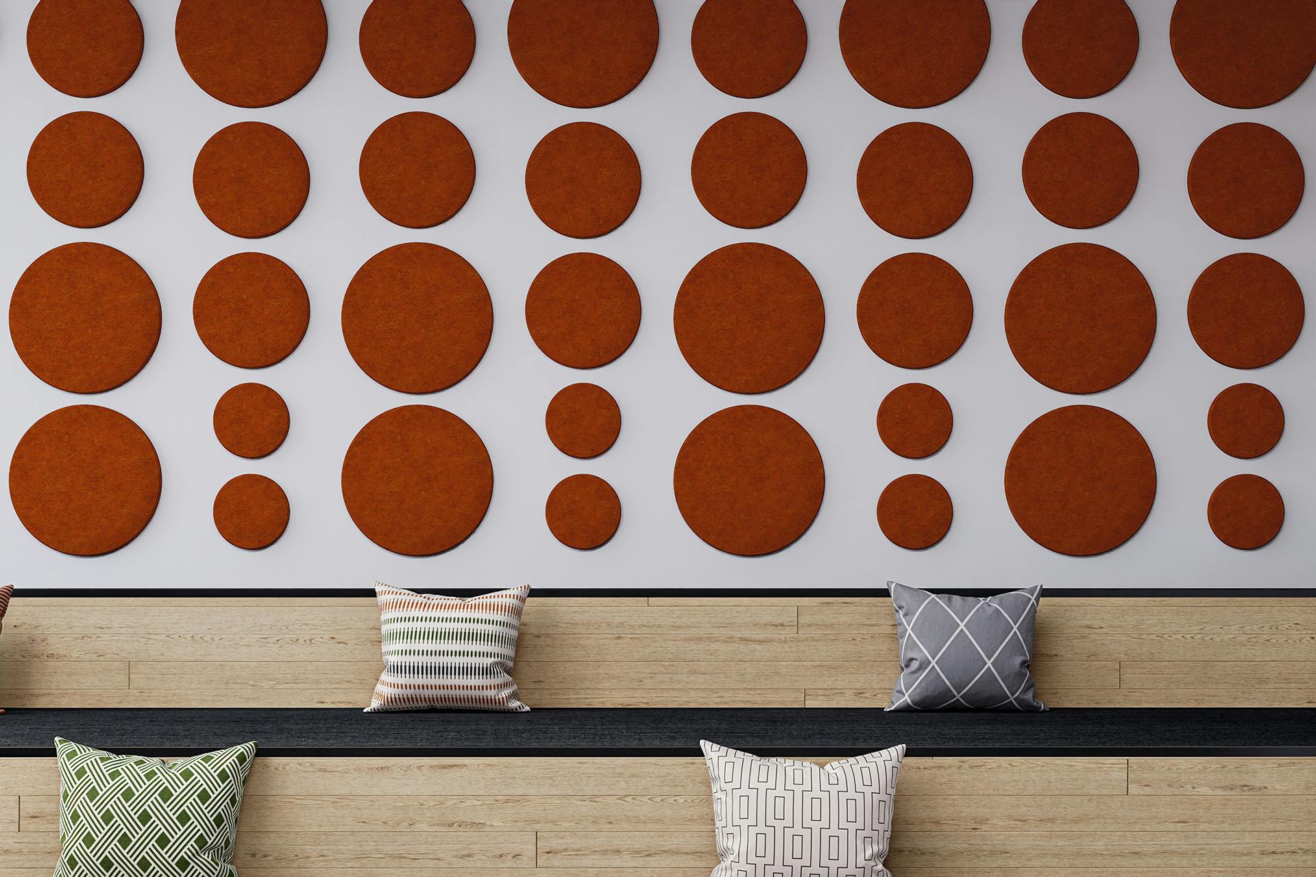 A modern interior features a white wall adorned with multiple rust-colored acoustic felt circular panels of varying sizes. Below, there is a long wooden bench with black cushions, decorated with patterned throw pillows in grey, beige, and green.