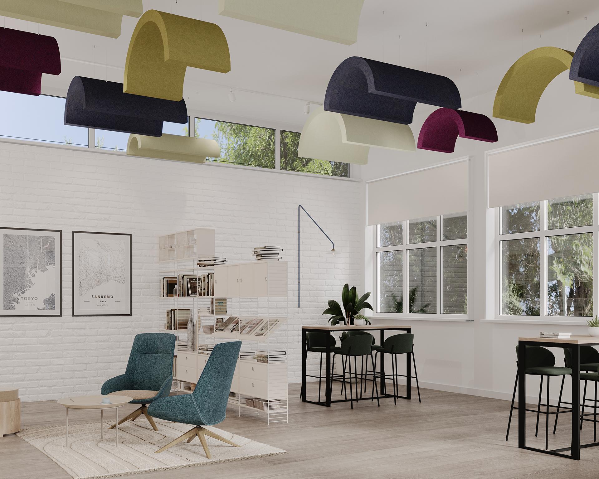 A modern office space with colorful, curved acoustic felt ceiling clouds, a white brick wall with framed maps, shelves filled with books and decor, and two green chairs around a coffee table. Large windows allow natural light, while a table with barstools sits near the windows.